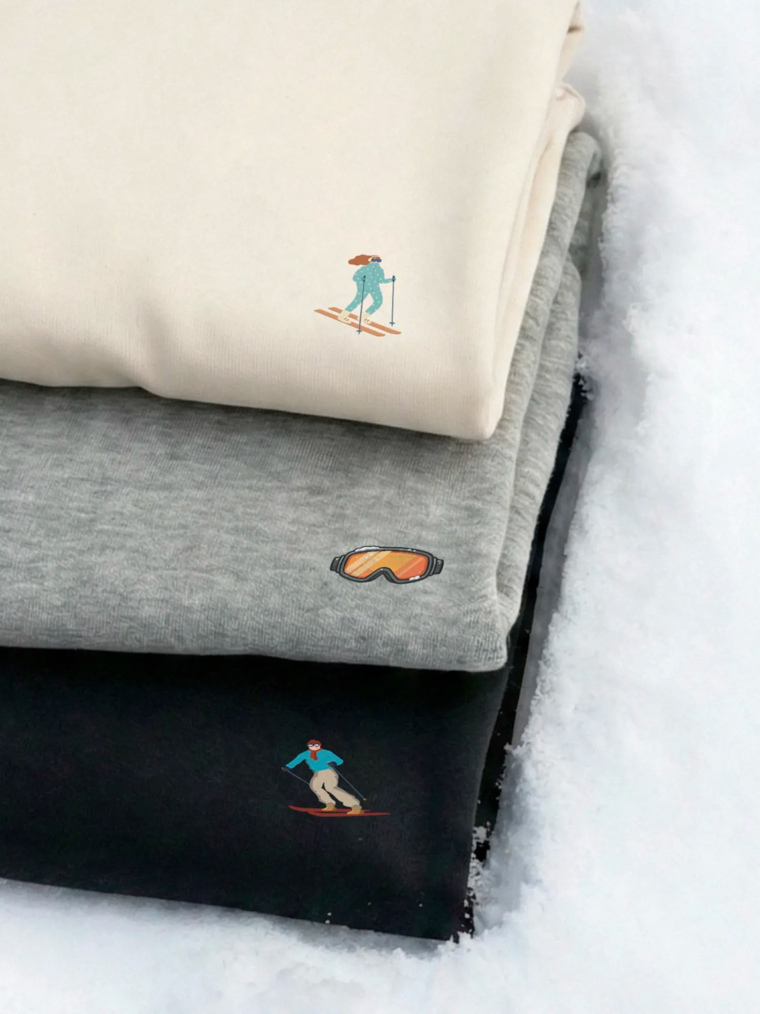 Stack of 3 sweatshirts, off white, gray and black with designs from the Down The Slopes Minis collection by inspire.inc